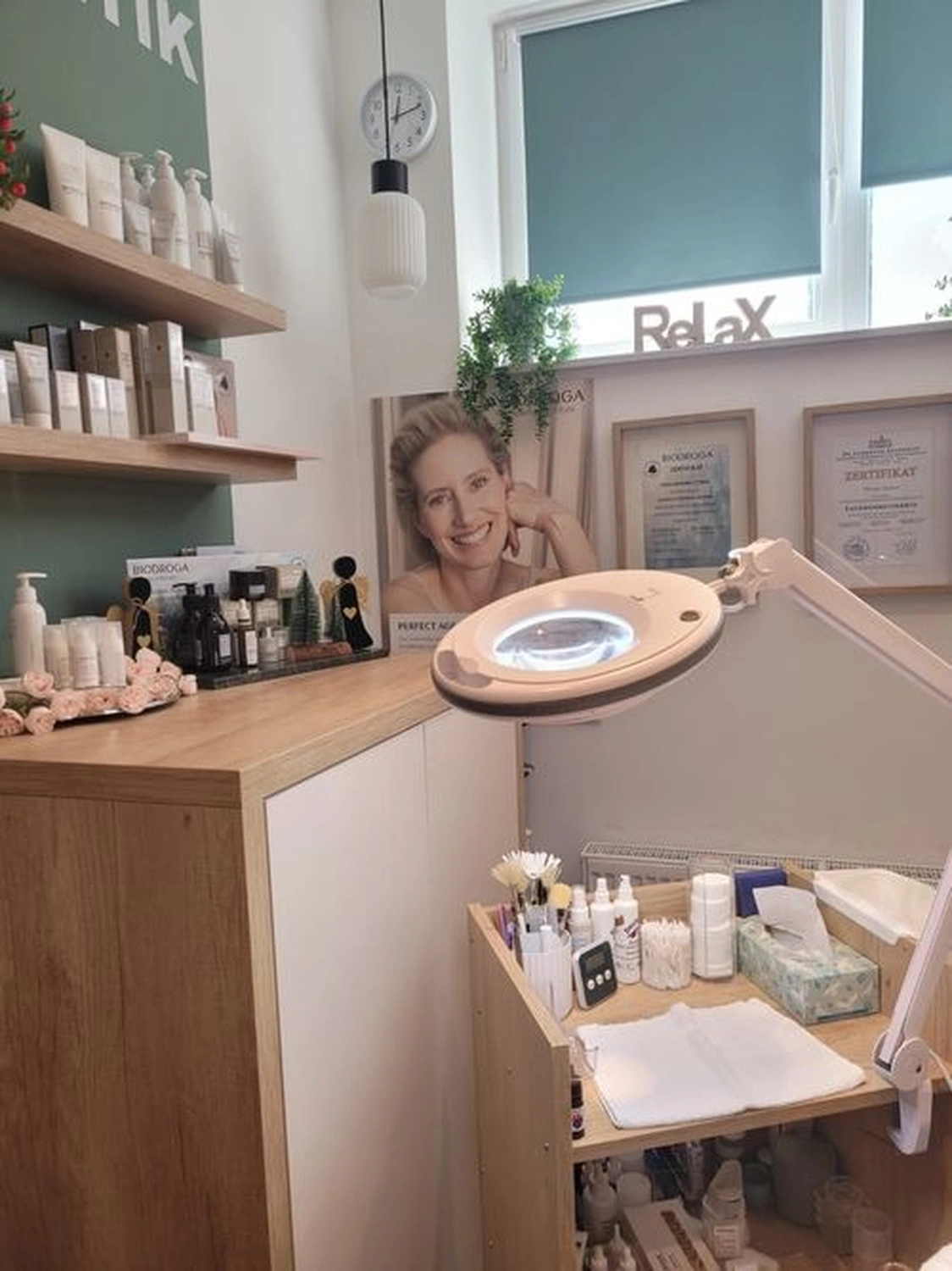 Marina Litwin - Behandlungen für Gesicht, Körper, Hände und Füße - Eine hell erleuchtete, moderne Hautpflegeklinik oder ein Schönheitssalon mit Holzregalen, die mit professionellen Produkten bestückt sind, einer Vergrößerungslampe über einem Servierwagen und gerahmten Zertifikaten an der Wand.